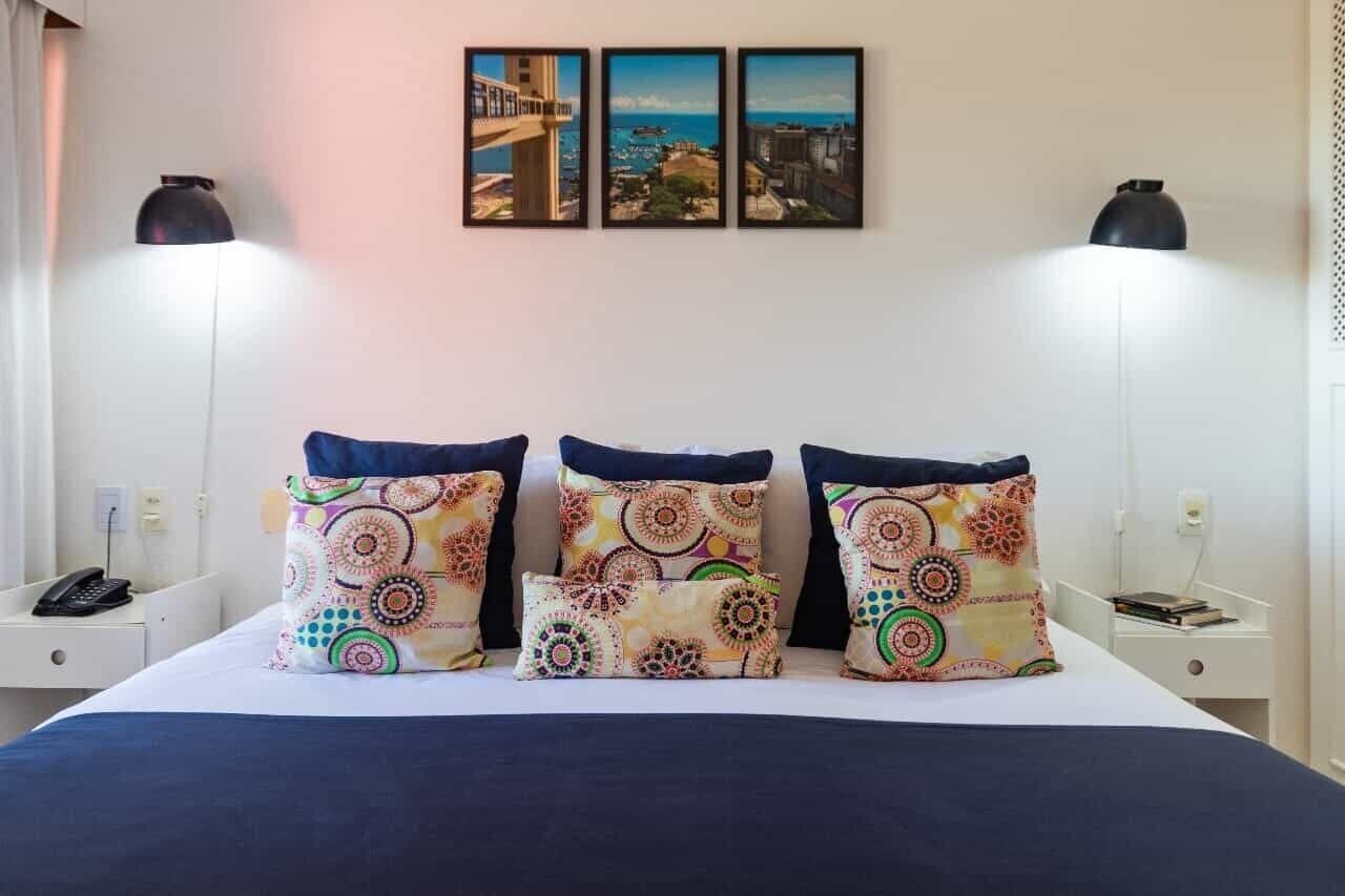 Habitación de hotel con una cama, tres almohadillas decorativas, una mesita de noche con teléfono y lámparas de pared.