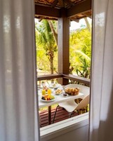 Mesa de desayuno con diversos alimentos y vistas a exuberante follaje exterior.