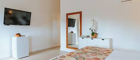 A modern bedroom with a bed, a television, a small refrigerator, a dresser, and a mirror.