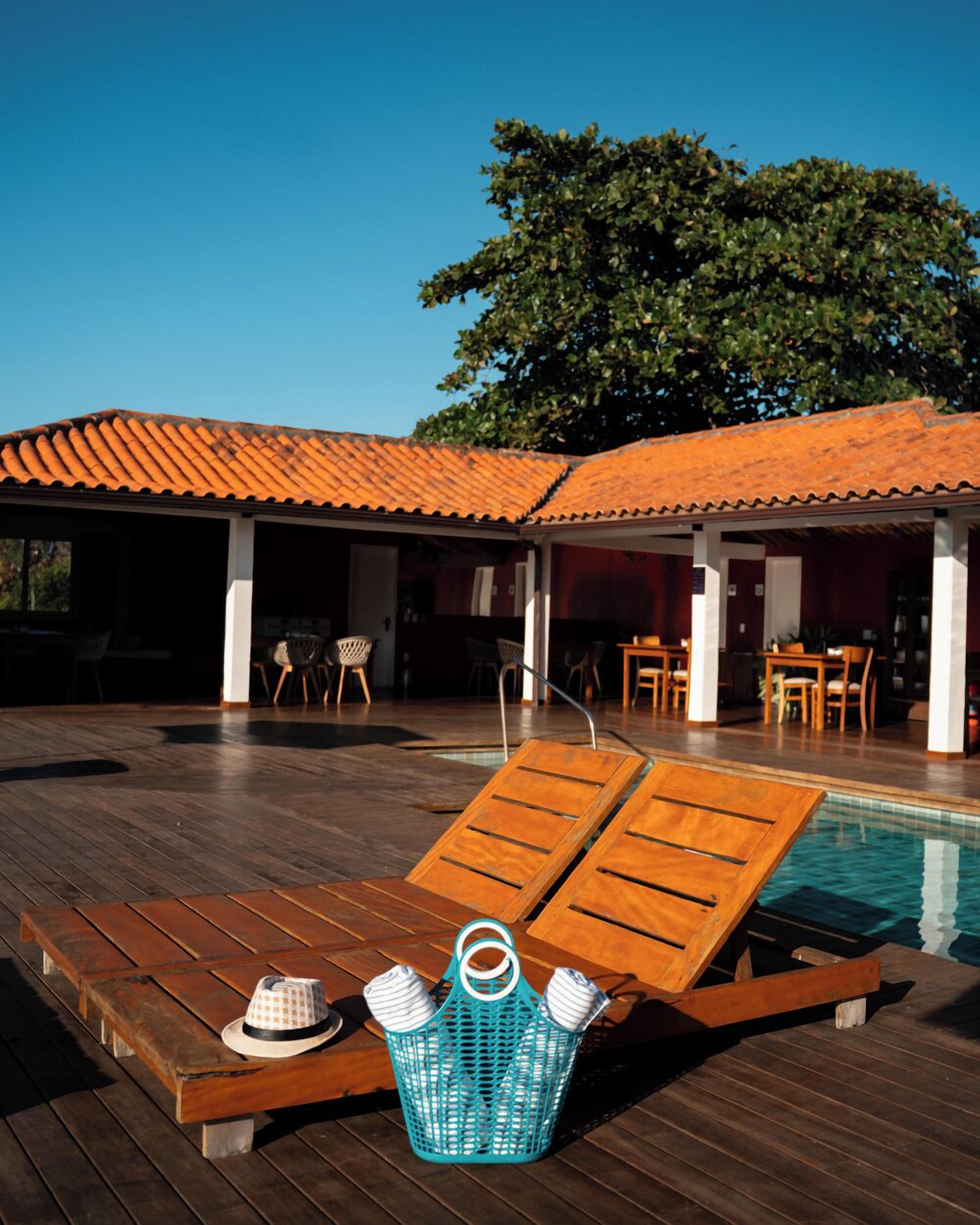 A wooden deck with lounge chairs, a pool, and a covered area with tables and chairs.