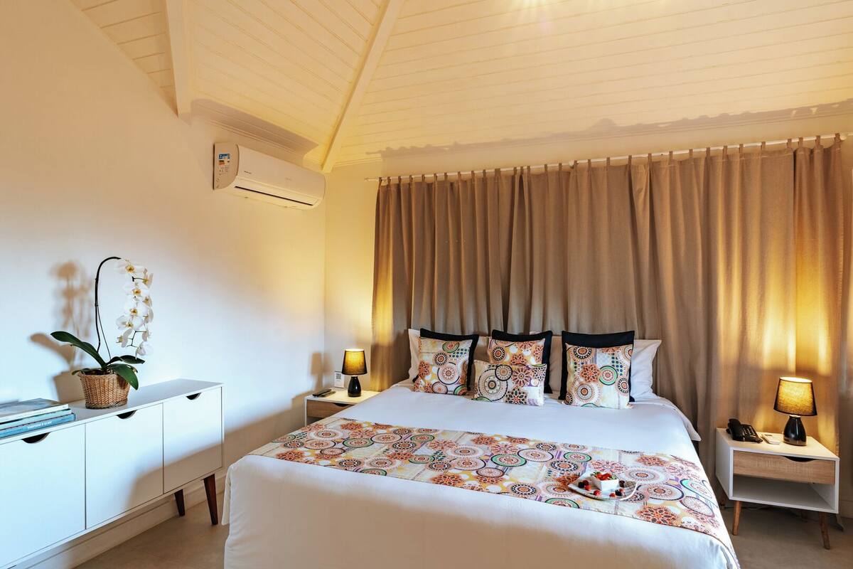 Habitación de hotel con cama, dos mesitas de noche con lámparas, cómoda y aire acondicionado, además de una ventana con cortinas.