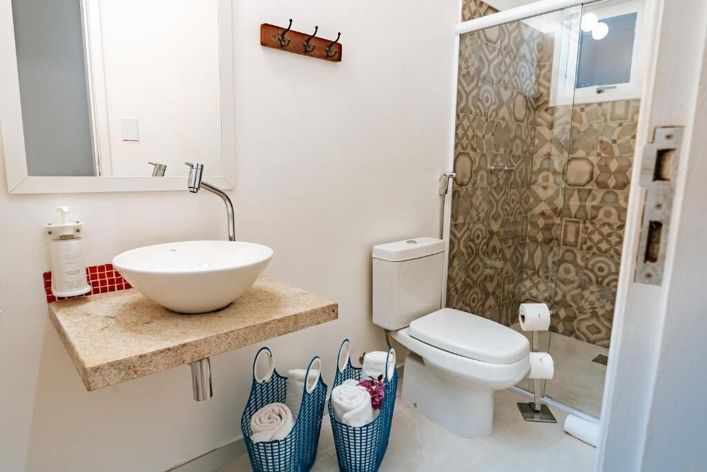 A bathroom with a white sink, a toilet, and a shower area. There are two blue baskets with towels and toiletries.