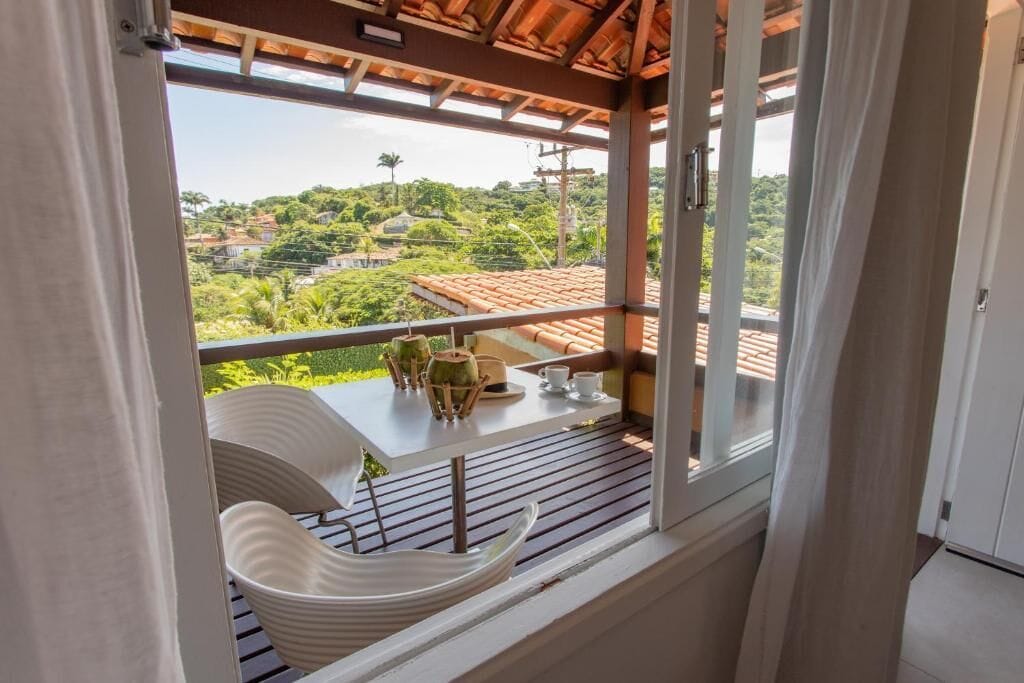 A balcony with a table and chairs, overlooking a lush green landscape with houses.