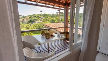 A balcony with a table and chairs, overlooking a lush green landscape with houses.