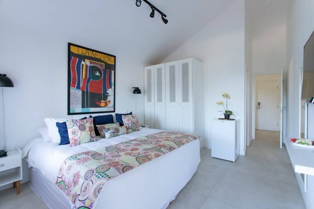 A modern bedroom with a large bed, white wardrobe, and a painting on the wall.