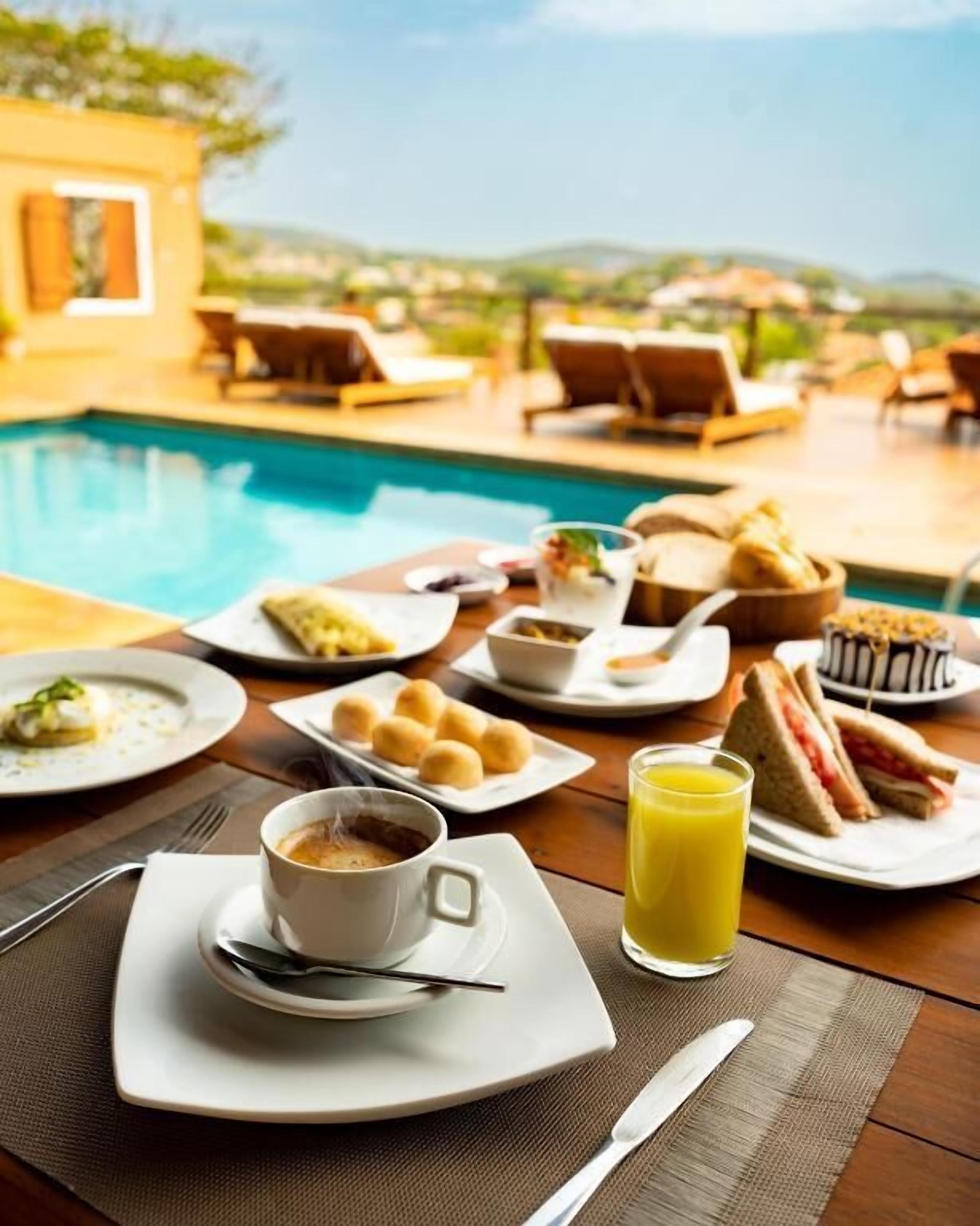 A breakfast setting by a pool with plates of food, a cup of coffee, and a glass of orange juice.