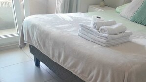 Una cama bien hecha con cubrecama blanco y toallas blancas dobladas.