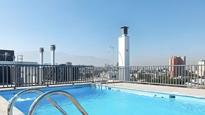Una piscina en la azotea con barandilla de metal, agua azul cristalina y un paisaje urbano de fondo.