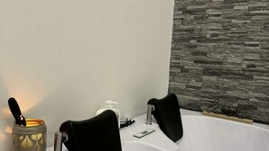 Un baño moderno con una bañera blanca, asientos de baño negros, un cabezal de ducha manual y un candelabro decorativo.