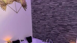 Un baño moderno con una bañera independiente, pared de piedra y decoración mural.