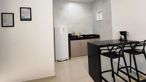 A modern kitchen with a black countertop, white cabinets, and a refrigerator. There is a coffee maker on the counter and a framed picture on the wall. - Búzios Suíte Home (Búzios)