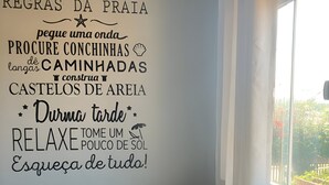A room with a wall decorated with motivational phrases in Portuguese, a round wooden table, and a view of greenery outside. - Búzios Suíte Home (Búzios)