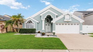 A two-story house with a light blue exterior, a white garage door, and a well-maintained front lawn. - Fascinating private pool and game-room, near Disney!! (Kissimmee)