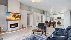 A modern living room with a fireplace, a large TV, and a dining area with chairs. - Fascinating private pool and game-room, near Disney!! (Kissimmee)