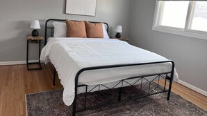 Un dormitorio con una cama, dos mesitas de noche, un ventanal con persianas y una alfombra estampada.