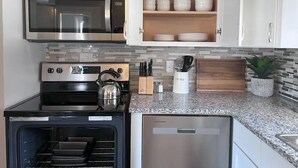Cocina moderna con microondas integrado, horno y lavavajillas, armarios de madera y salpicadero de azulejos.