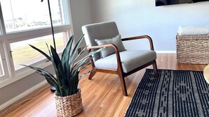 Una sala de estar moderna con un sillón gris, una maceta tejida, un tapete con estampado blanco y negro, y una lámpara de pie.