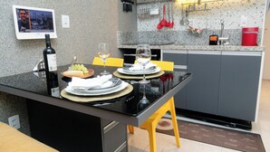 A modern kitchen with a black countertop, yellow stools, and a dining table set for two. - Flat Vip 5 Estrelas (Cotia)
