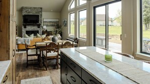 A spacious kitchen with a stone fireplace, large windows, and a view of the backyard. - NEW charming 3 bedroom cottage nestled on the scenic Red Lodge Golf Course  (Red Lodge)
