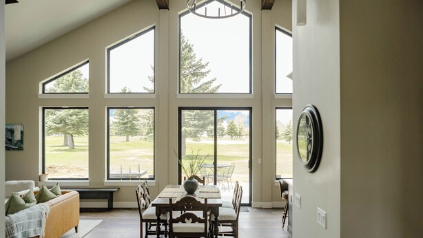 A dining area with a table and chairs, large windows offering a view of a grassy landscape, and a clock on the wall. - NEW charming 3 bedroom cottage nestled on the scenic Red Lodge Golf Course  (Red Lodge)