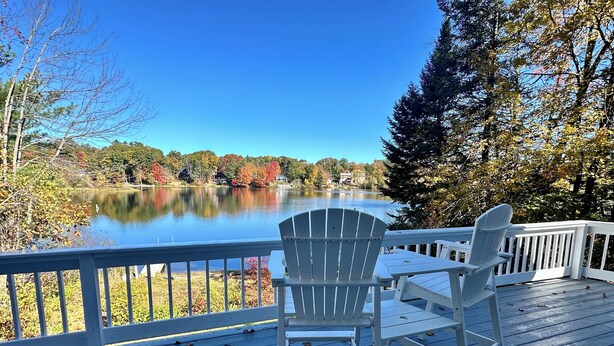 A deck with two Adirondack chairs overlooking a lake with autumn foliage. - Lakefront home with hot tub, beach, skiing nearby in tranquil Barnstead (Barnstead)