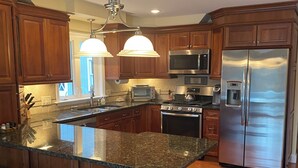 A modern kitchen with wooden cabinets, stainless steel appliances, a granite countertop, and bar stools. - Lakefront home with hot tub, beach, skiing nearby in tranquil Barnstead (Barnstead)