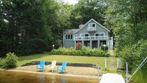 A house with a dock extending into a body of water, surrounded by greenery. - Lakefront home with hot tub, beach, skiing nearby in tranquil Barnstead (Barnstead)