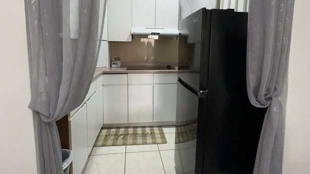 Une cuisine de taille réduite avec des meubles blancs, un réfrigérateur noir et un sol carrelé.