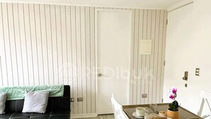 Uma sala de estar moderna com um sofá preto, almofadas brancas e uma mesa de jantar posta com pratos, xícaras e um vaso com flores.