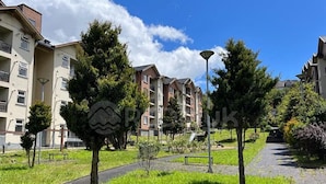 Área residencial com edifícios de apartamentos, um caminho pavimentado e uma placa com o símbolo de uma montanha.