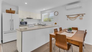 Una cocina moderna con armarios blancos, una isla central y un comedor con mesa y sillas de madera.