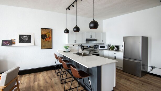 A modern kitchen with a central island, bar stools, a stainless steel refrigerator, and pendant lighting. - Cozy studio in enchanting downtown Warrensburg with full kitchen, AC, WiFi (Warrensburg)