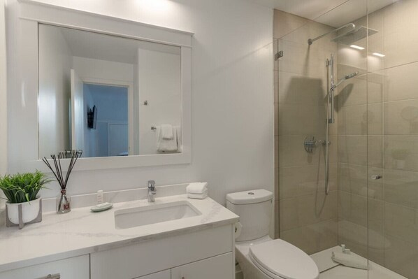 Une salle de bain moderne avec un grand miroir, un lavabo, des toilettes et une douche à parois de verre.