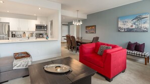 Ein modernes Wohnzimmer mit einem roten Sofa, einem Essbereich mit einer Chandelieber und einer Küche mit weißen Schränken.