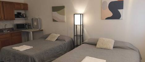 Een kamer met twee bedden, een kitchenette, een ventilatorkachel en abstracte wanddecoratie.