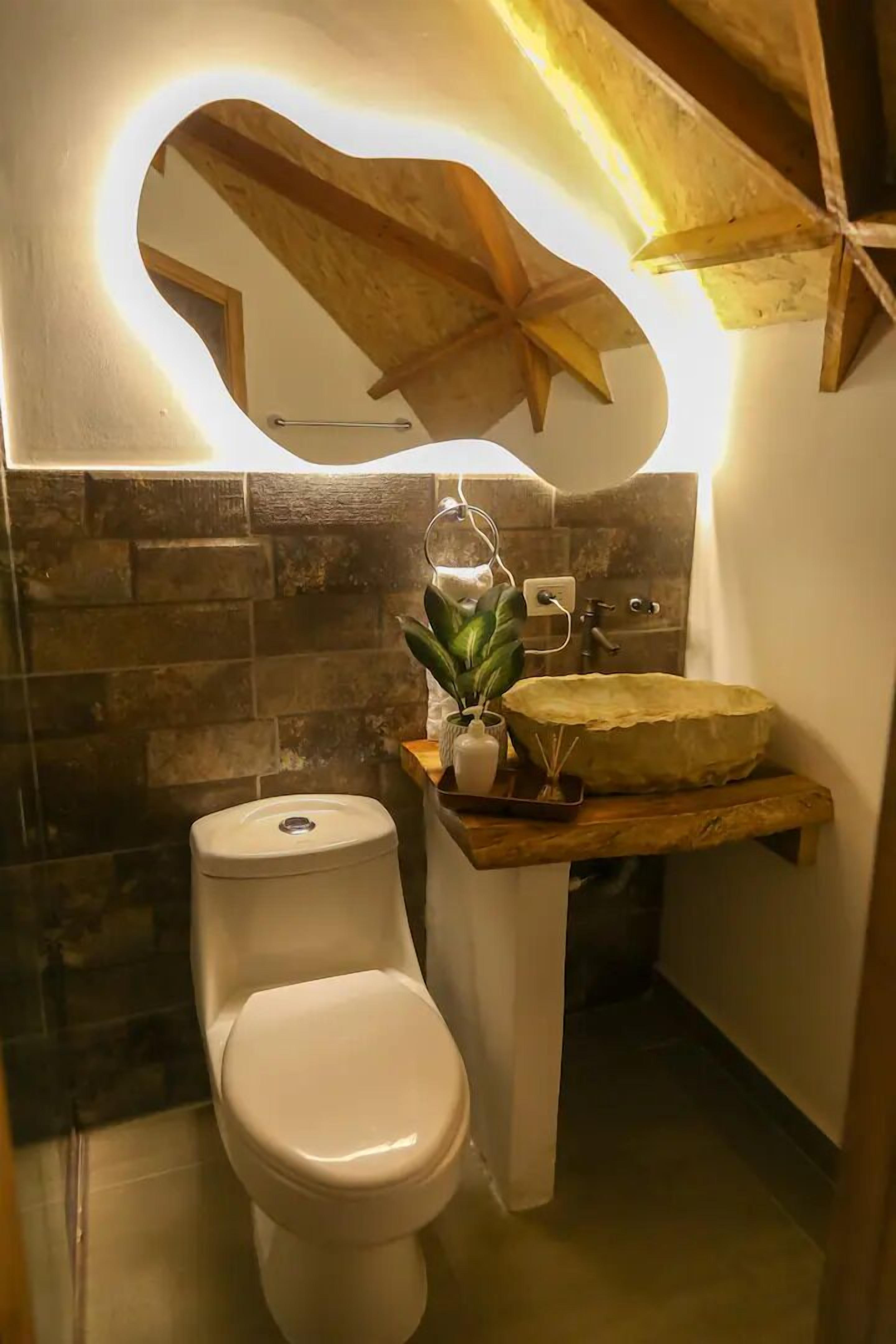 A modern bathroom with a stone tile backsplash, a wooden ceiling, and a unique curved mirror above the sink.