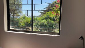 A bedroom with a bed, a window with a view of greenery, and a bedside table with a lamp. - Detached, fully furnished cabin with a terrace and barbecue, just steps from Playa Negra, (Concón)