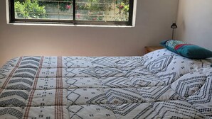 A bedroom with a bed, a window with a view of greenery, and a bedside lamp. - Detached, fully furnished cabin with a terrace and barbecue, just steps from Playa Negra, (Concón)