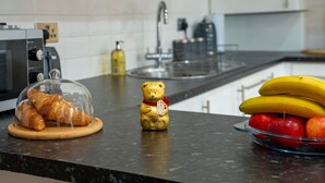 Una encimera de cocina con cruasanes, un oso de peluche, plátanos y manzanas.