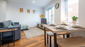 Una sala de estar moderna con un sofá gris, una mesita de madera y un comedor con mesa puesta.