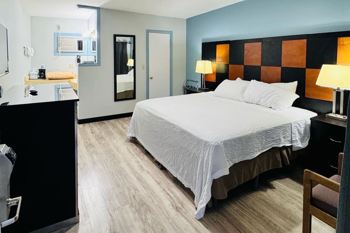 Hotellihuone, jossa on sänky, yöpöytälamput, työpöytä ja peili.