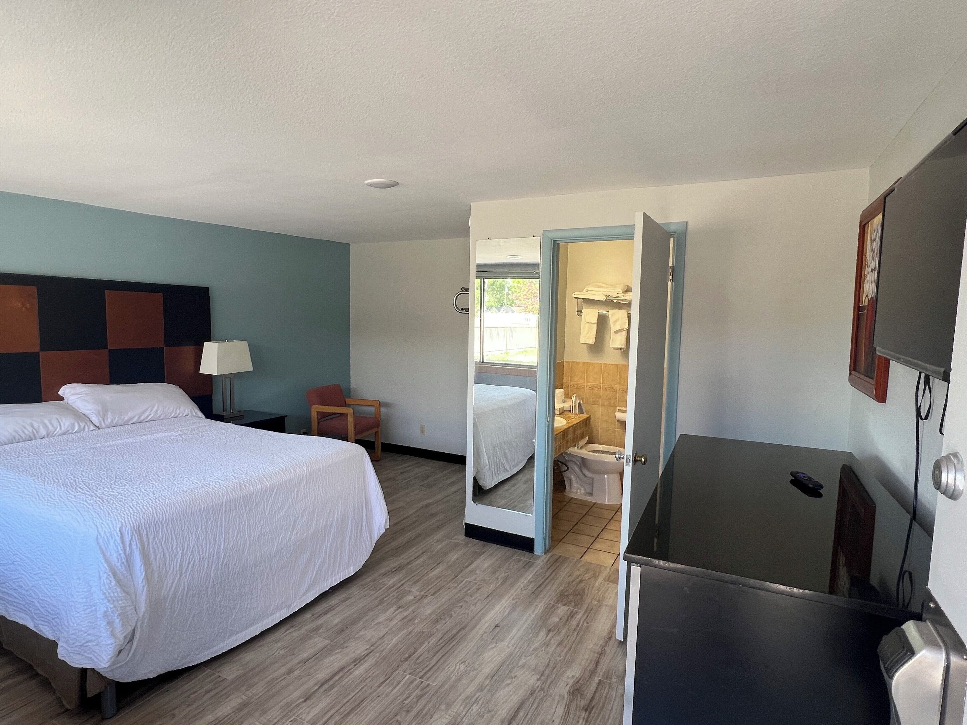 A hotel room with a bed, a desk, a chair, and a bathroom visible through an open door.