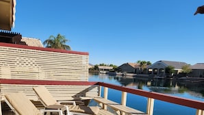 Una terraza de madera con sillones de descanso y vistas a un cuerpo de agua tranquilo y edificios al fondo.