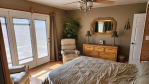 Un dormitorio con una cama, una silla, un tocador, un espejo y un ventilador de techo.