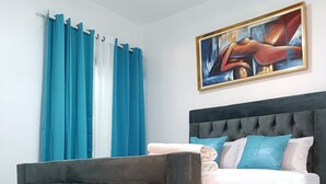 A bedroom with a dark grey tufted headboard, a bed with white and blue bedding, and a painting on the wall.