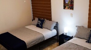 Two single beds with pillows and blankets, a bedside table, and a lamp.