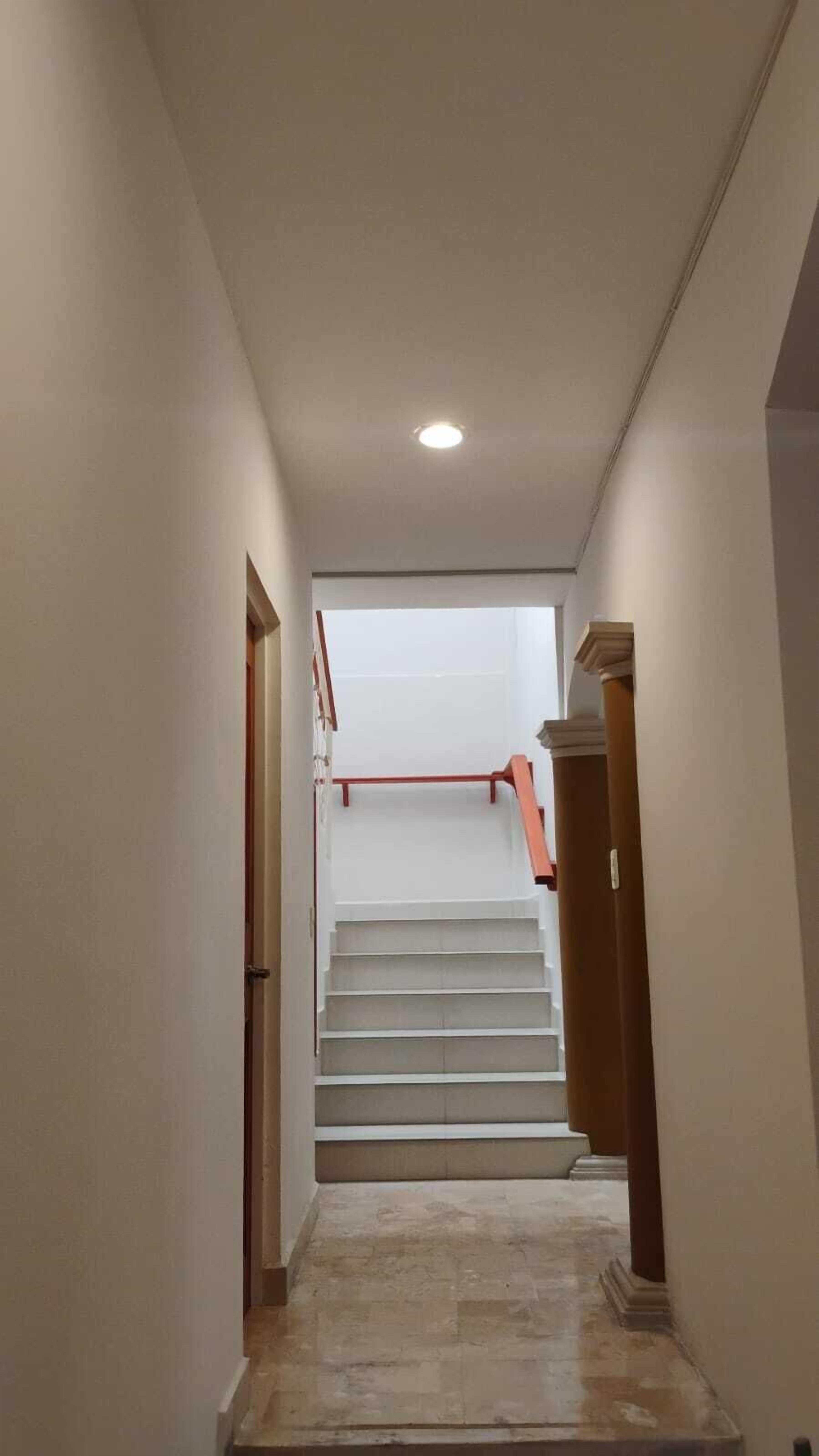 A narrow, well-lit hallway with a staircase leading to a landing.