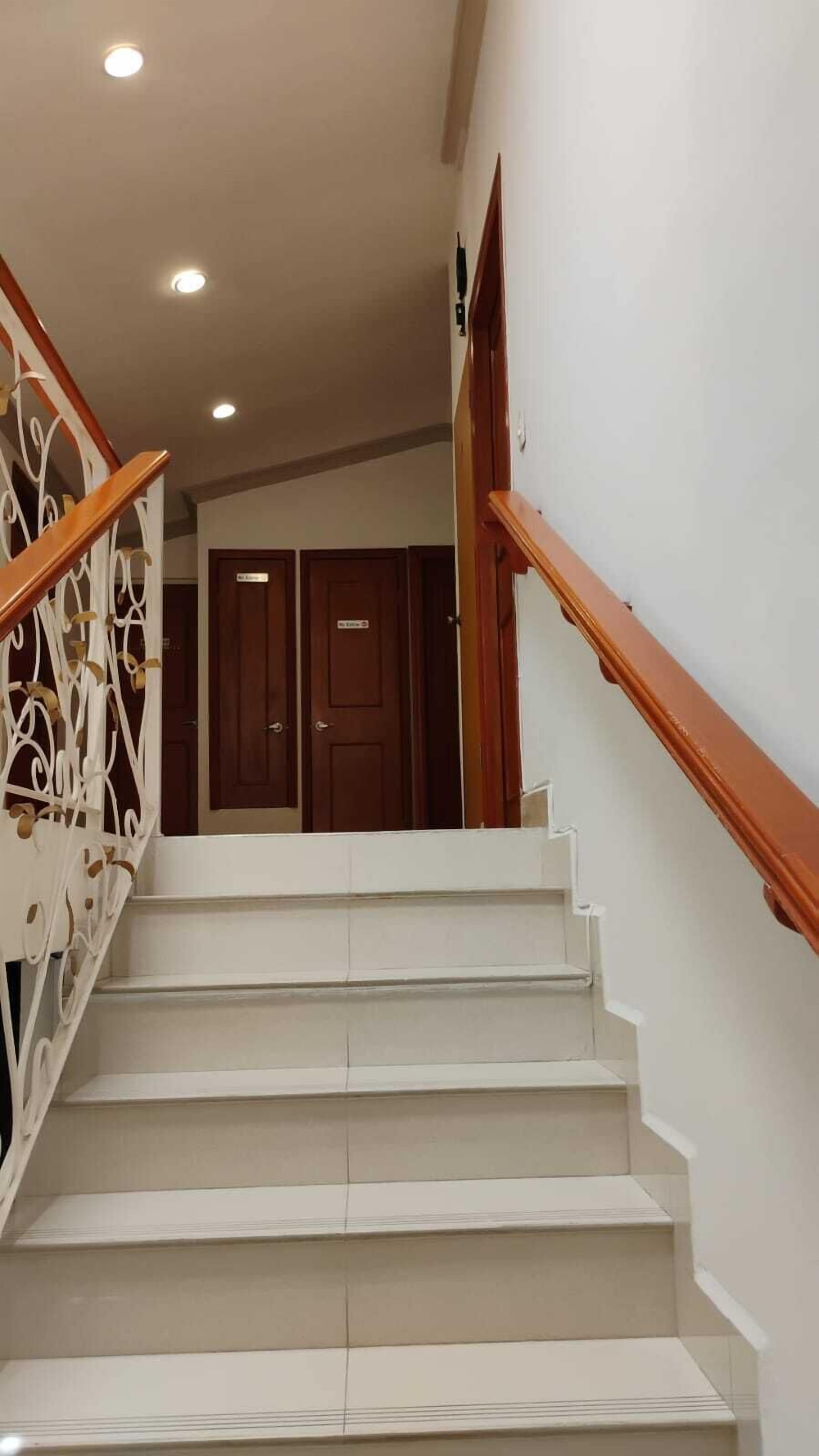 A staircase with white steps and wooden handrails, leading to a door with a sign above it.
