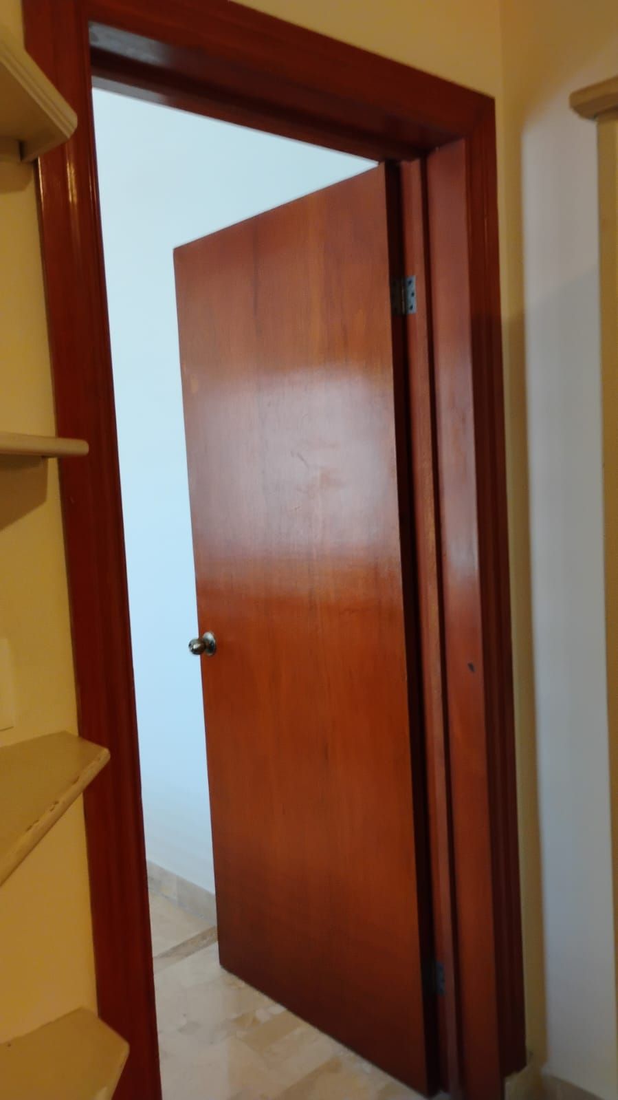 Une porte en bois avec une poignée en métal, une charnière visible et une petite plaque métallique fixée sur la porte.