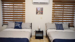 Una habitación con dos camas, cada una con cabecero de madera, una mesita de noche pequeña con lámpara y aire acondicionado instalado en la pared.